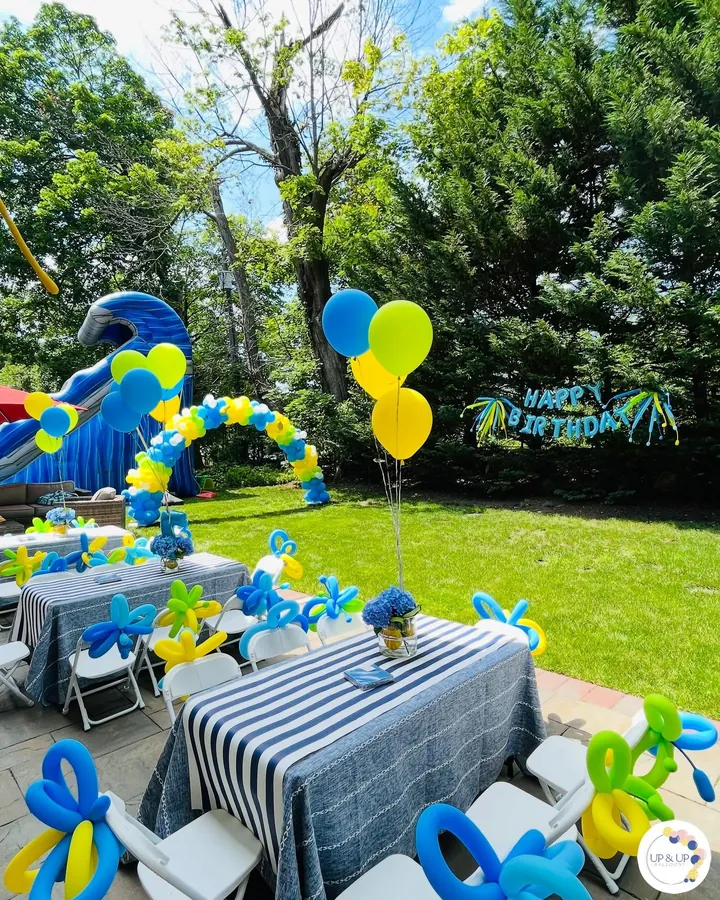 Backyard Birthday Bash: A blue, yellow and lime balloon arch, twisted-balloon chair bows and table bouquets for a summer party in the yard.